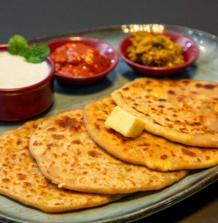 Appetizing Indian paratha served with yogurt and pickles on a blue plate.